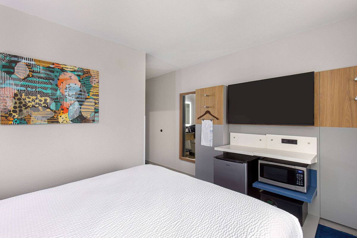 A hotel room with a bed, a painting, a microwave, and a small kitchenette.