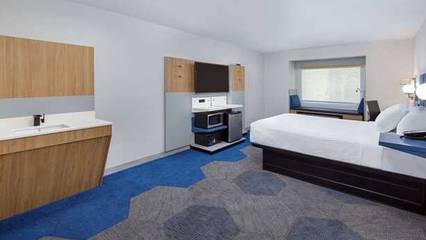 Une chambre d’hôtel équipée d’un lit, d’un bureau avec un ordinateur, d’un four à micro-ondes et d’une petite kitchenette.
