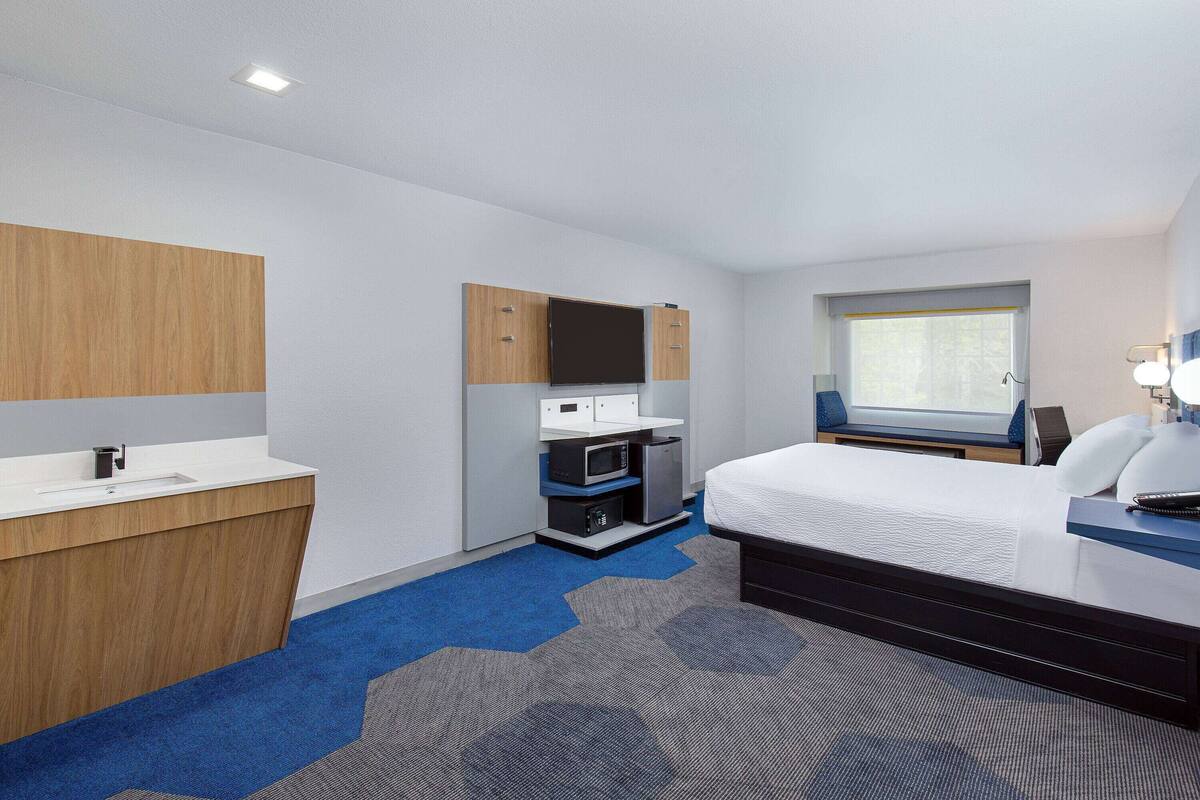 A hotel room with a bed, a desk with a computer, a microwave, and a small kitchenette.
