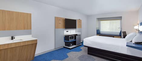 A hotel room with a bed, a desk with a computer, a microwave, and a small kitchenette.