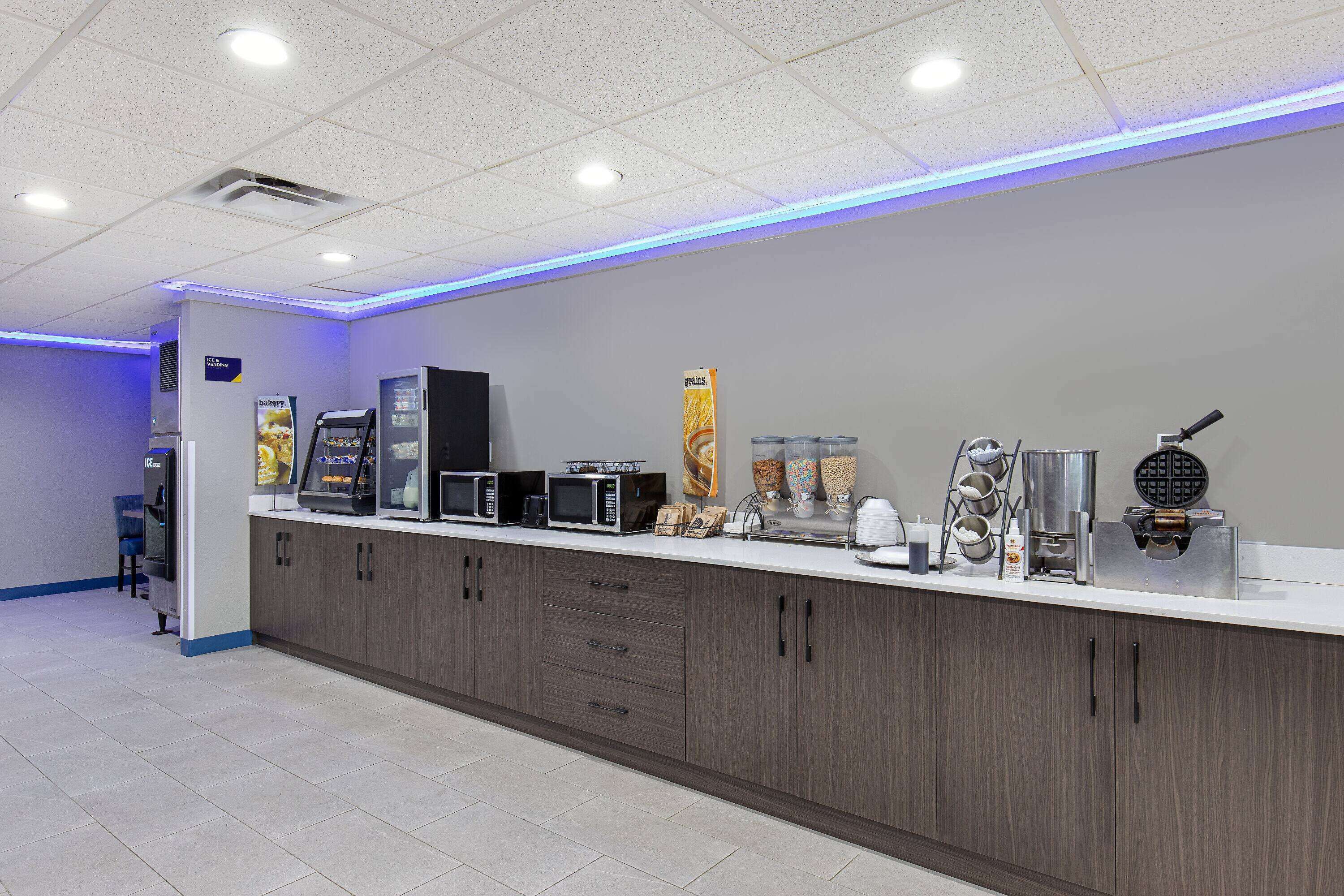 A self-service breakfast area with microwaves, coffee machines, and a waffle maker.