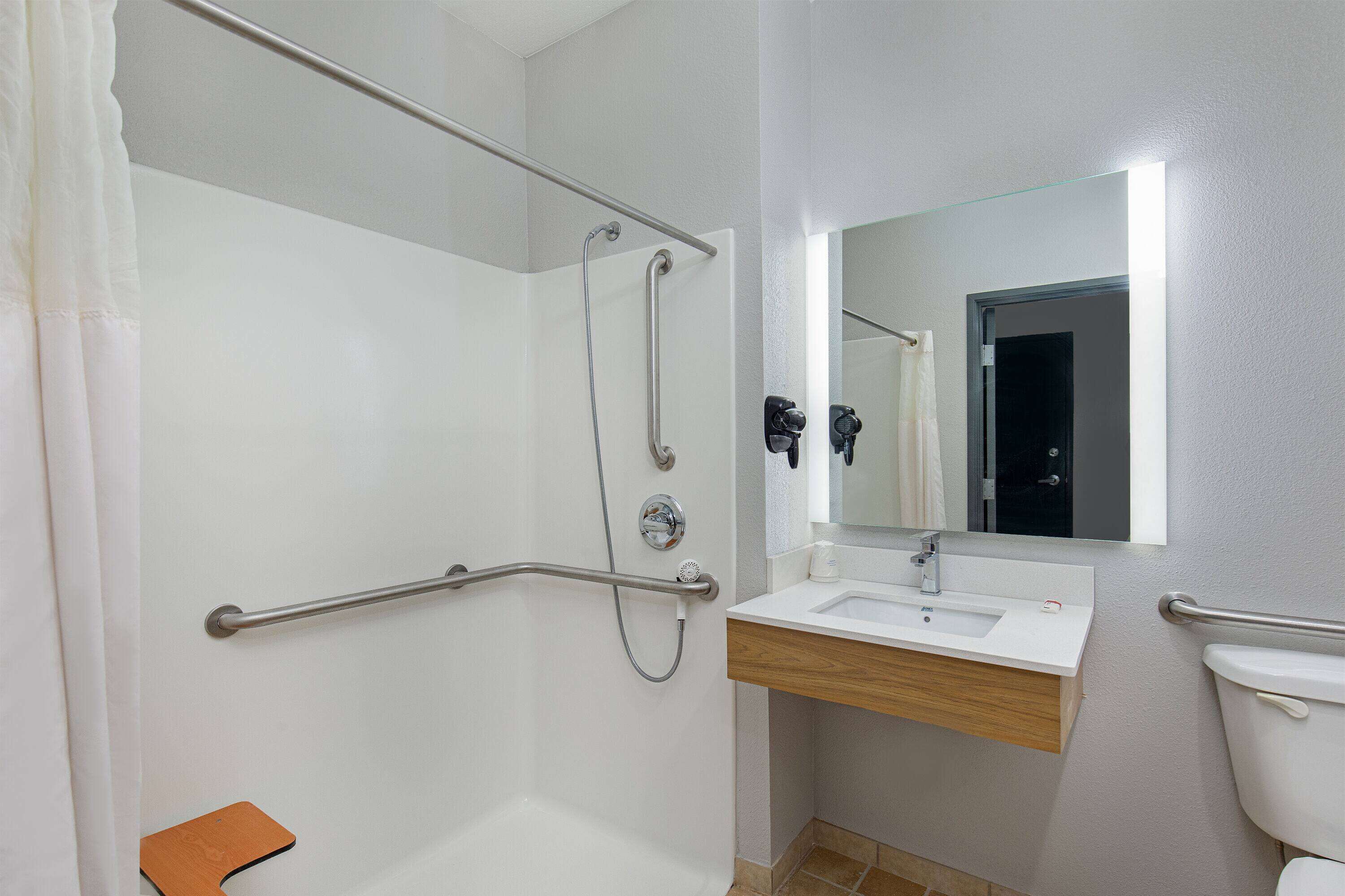 A bathroom with a shower, grab bars, a sink, and a toilet.