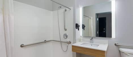 A bathroom with a shower, grab bars, a sink, and a toilet.