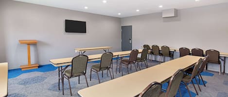 Une salle de conférence avec une longue table, des chaises, un pupitre et un téléviseur fixé au mur.
