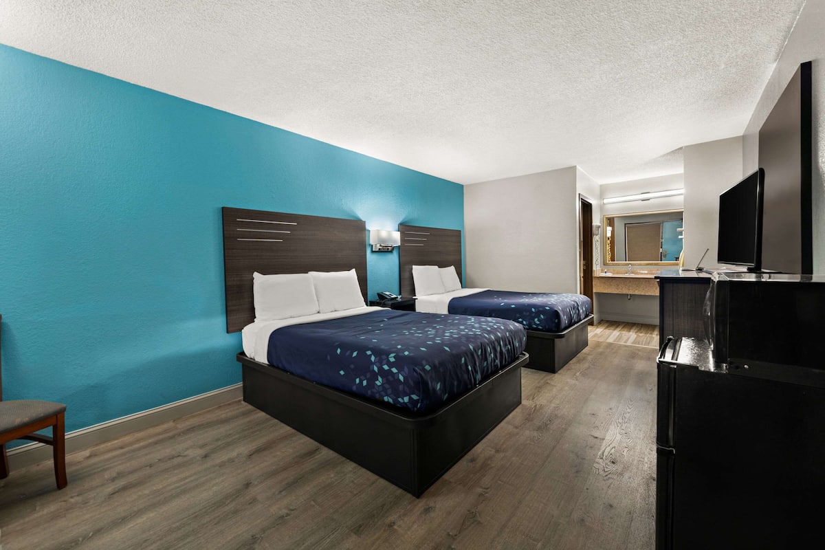 A hotel room with two beds, a TV, and a refrigerator.