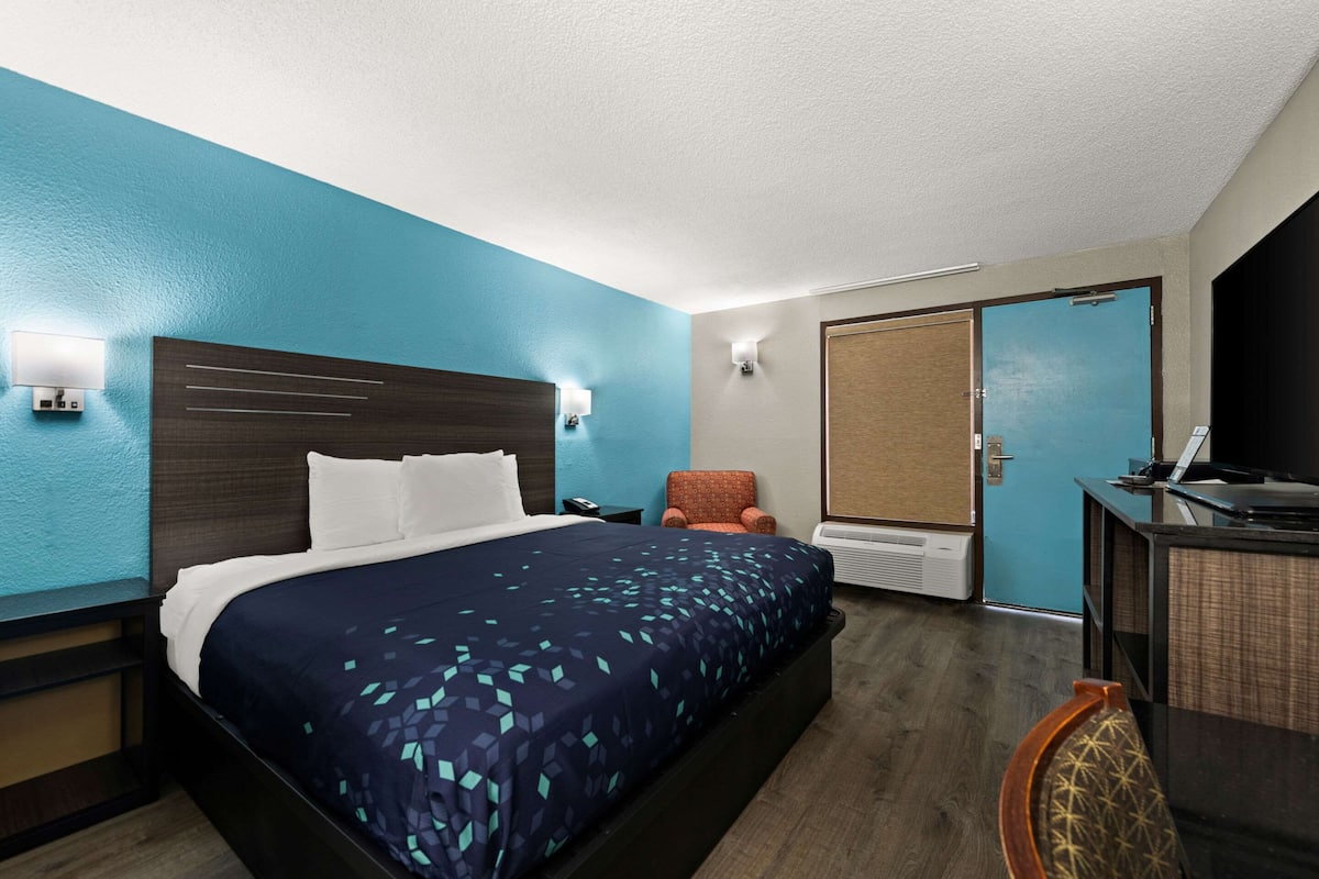 A hotel room with a bed, a desk, a chair, a wardrobe, and a door.