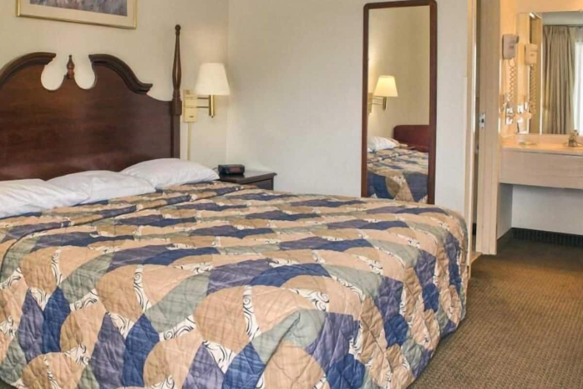 A hotel room with a large bed, a nightstand, a lamp, a mirror, and a bathroom visible through an open door.