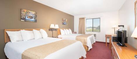 Una habitación de hotel con dos camas, un escritorio con televisor y una ventana con vistas.