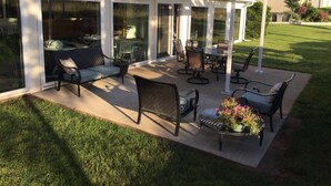 Un patio couvert aménagé avec du mobilier d’extérieur, notamment des chaises et une table, ainsi qu’un petit jardin fleuri.