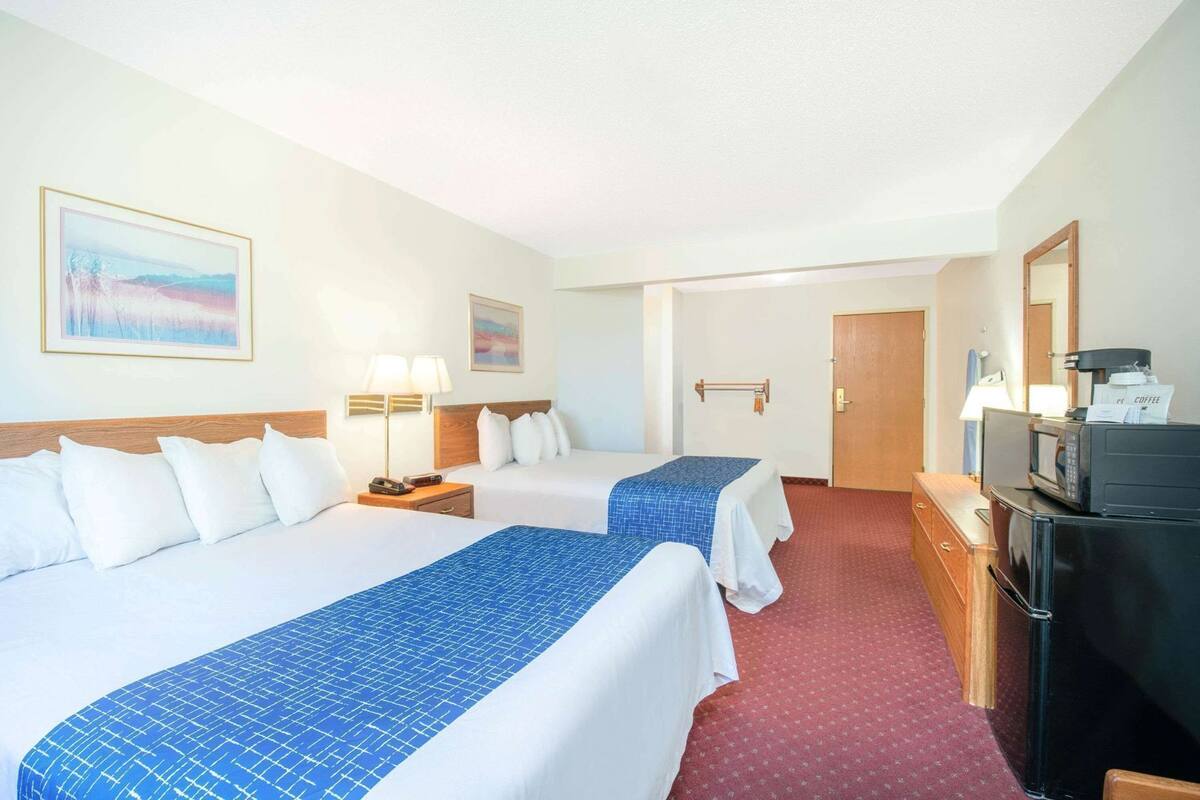 Une chambre d’hôtel avec deux lits, un bureau équipé d’un four à micro-ondes, d’une machine à café et d’une porte.