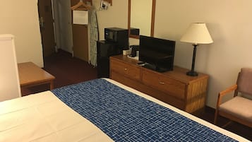 A hotel room with a bed, a wooden dresser, a television, a lamp, and a chair.