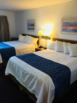 Une chambre d’hôtel avec deux lits, chacun étant équipé de draps blancs et d’une couvre-lit à motifs bleus. On y trouve une table de chevet avec une lampe et un téléphone.
