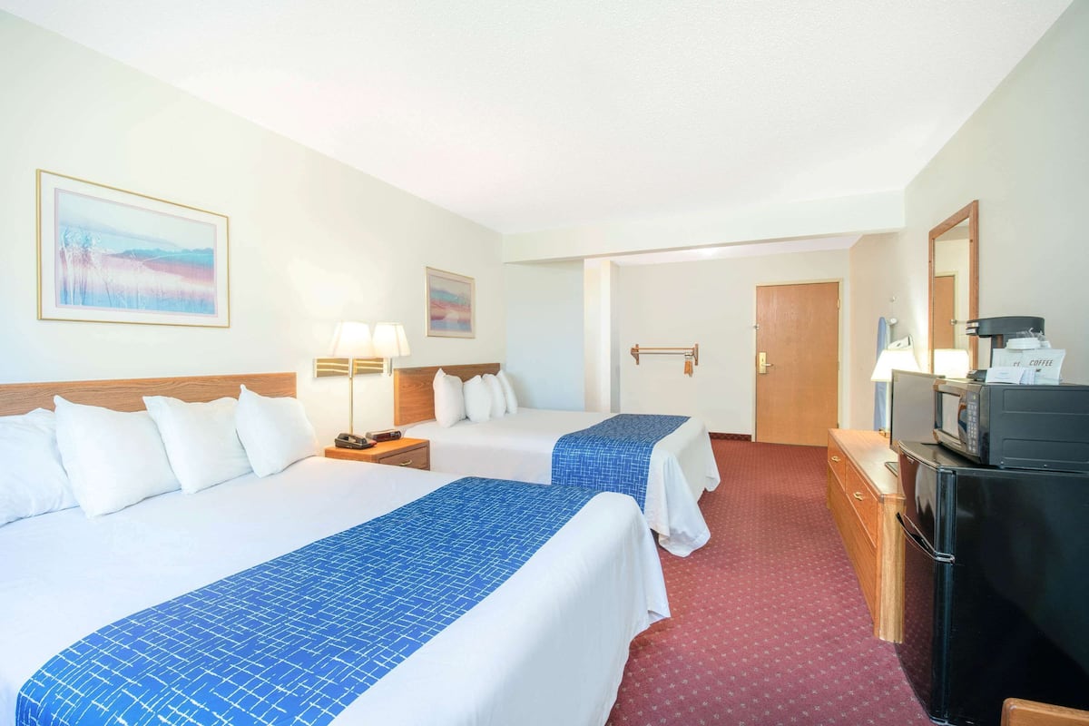 Une chambre d’hôtel avec deux lits, un bureau équipé d’un micro-ondes et une porte donnant sur une autre pièce.