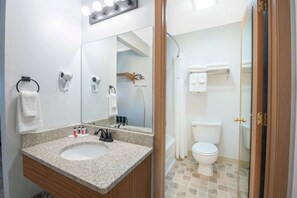 A bathroom with a granite countertop sink, a mirror, a towel rack, a handheld showerhead, and a toilet.