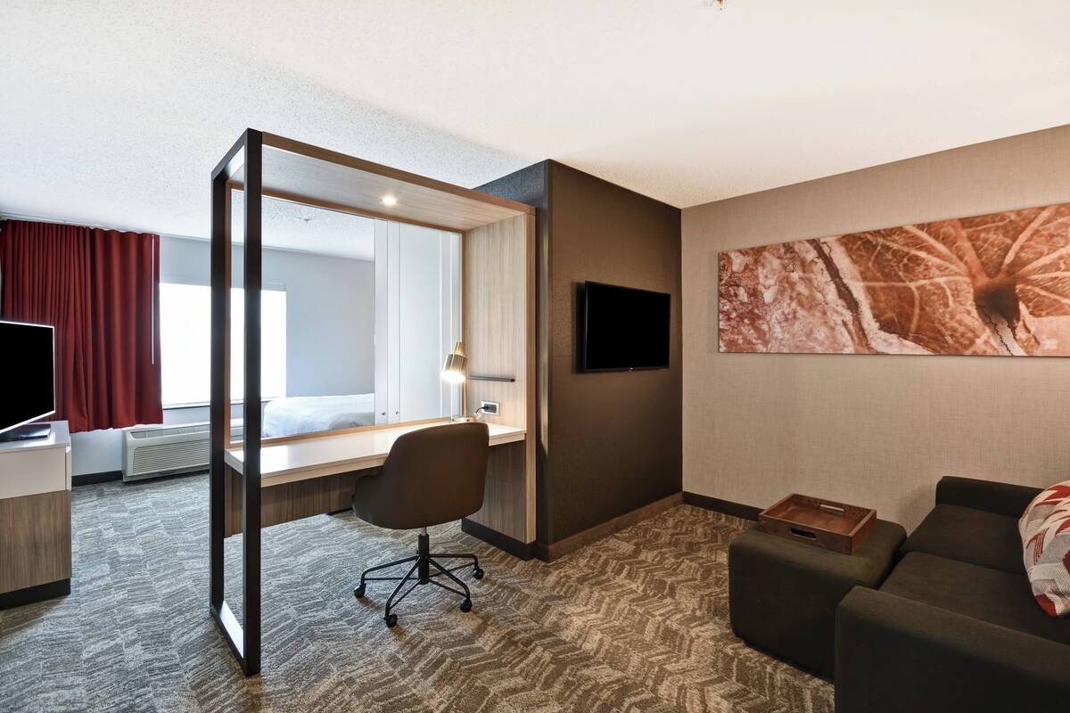 Ein Hotelzimmer mit Bett, Schreibtisch, Stuhl, Fernseher und einem großen Fenster.