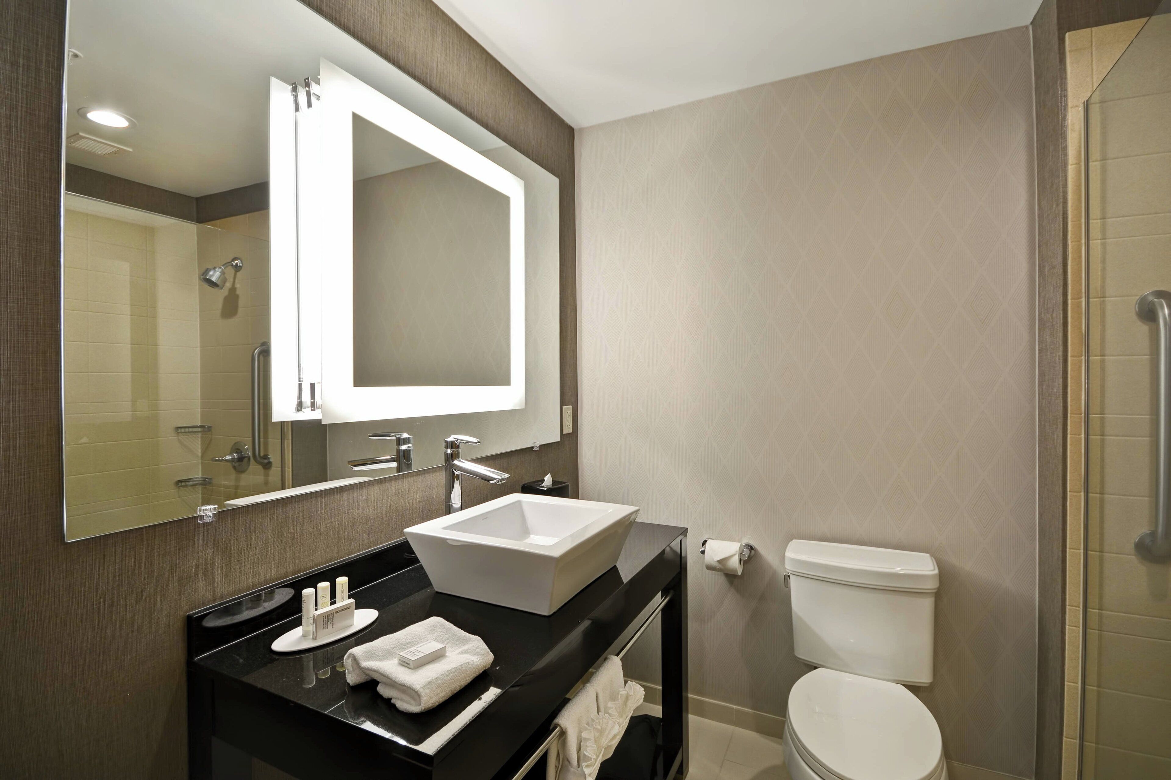 Une salle de bain moderne avec un grand miroir, un lavabo blanc, des toilettes et un espace douche.