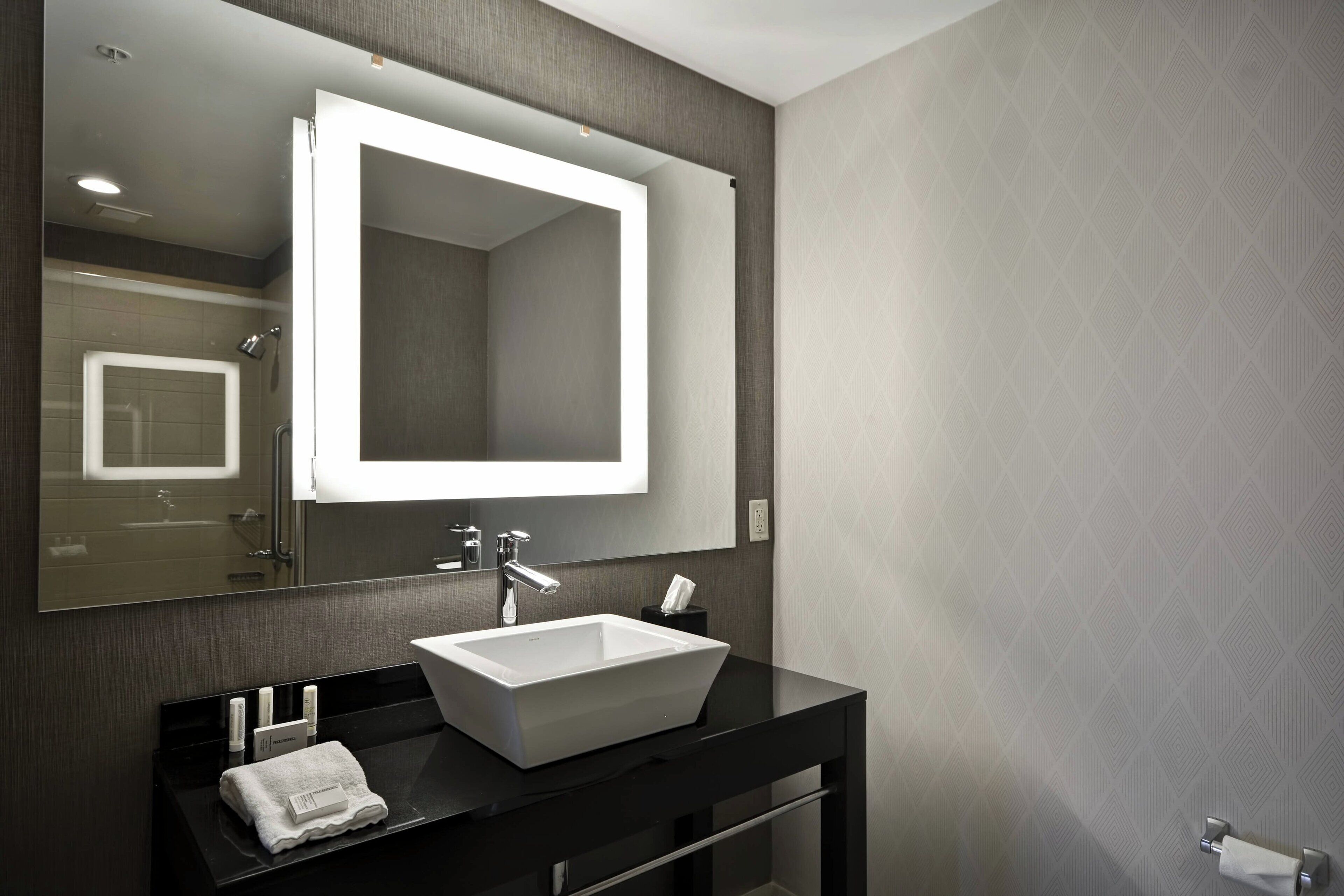 A modern bathroom with a large mirror, a white sink, and a black countertop.