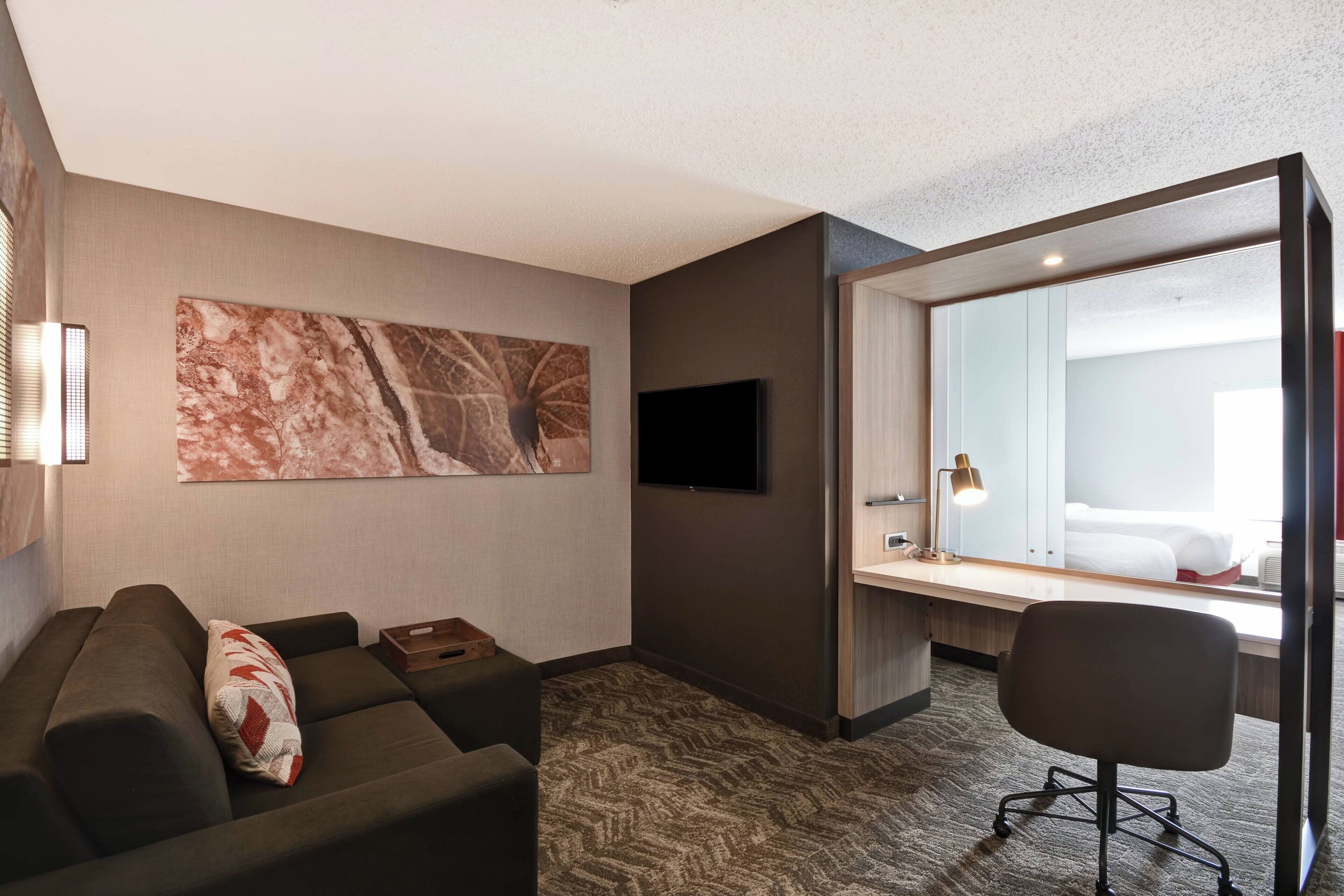 Een moderne hotelkamer met een bank, een bureau, een flatscreen televisie en een grote spiegel.