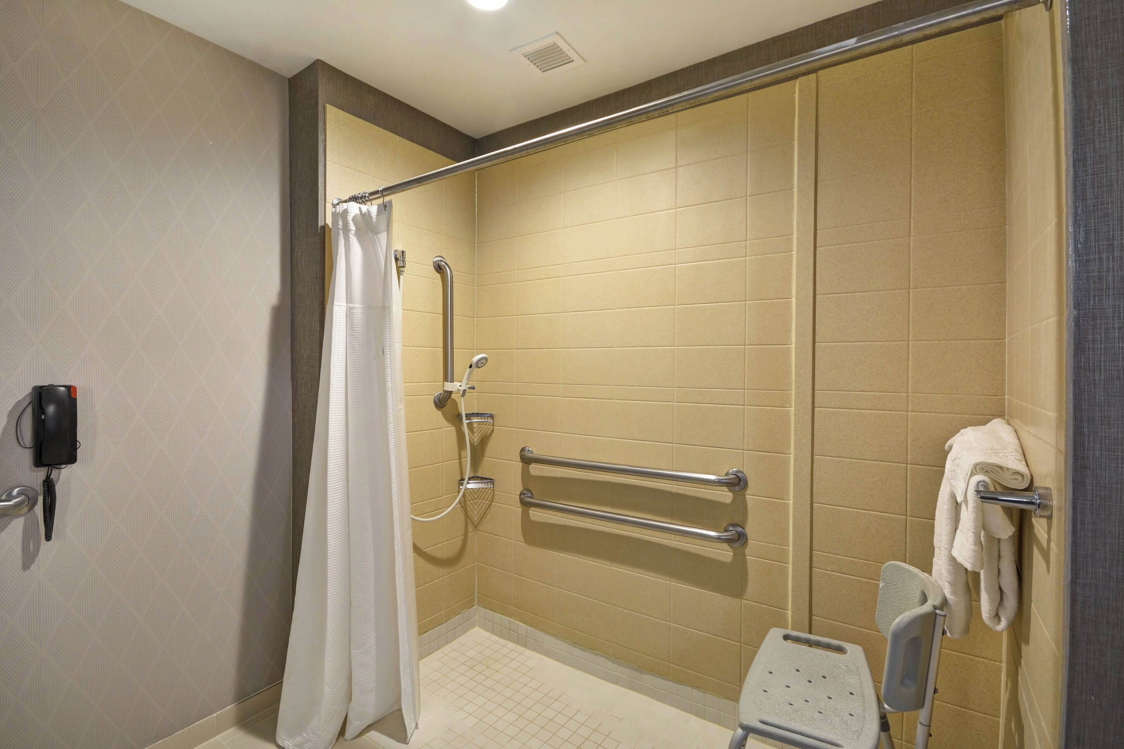A handicap-accessible shower with grab bars, a shower chair, and a towel rack.