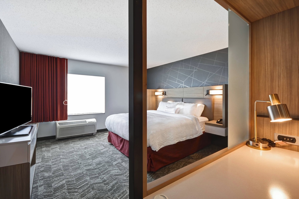 A hotel room with a bed, bedside table, lamp, and a large window with curtains.