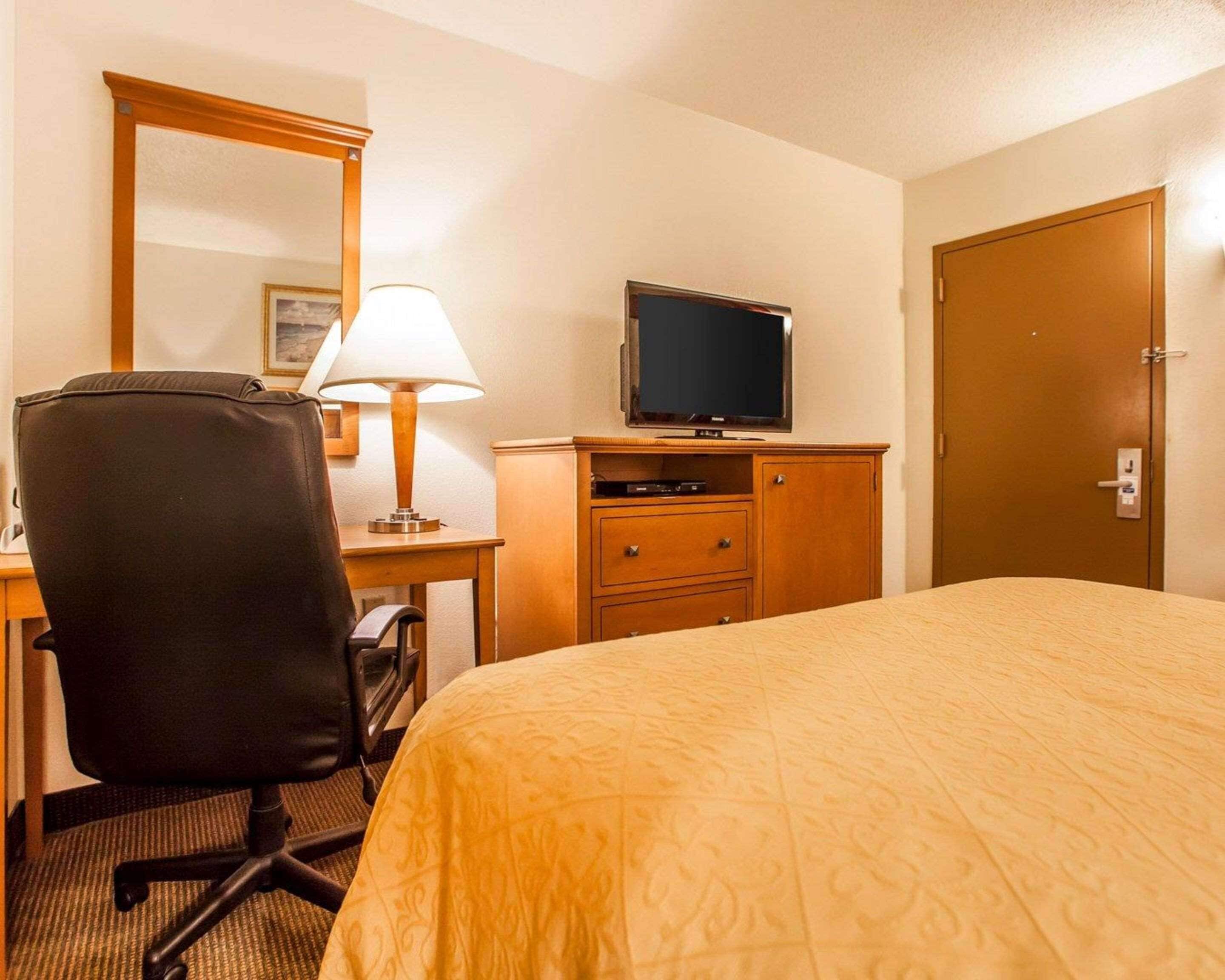 Ein Hotelzimmer mit einem Bett, einem Schreibtisch mit Stuhl, einem Fernseher, einer Kommode und einer Tür.