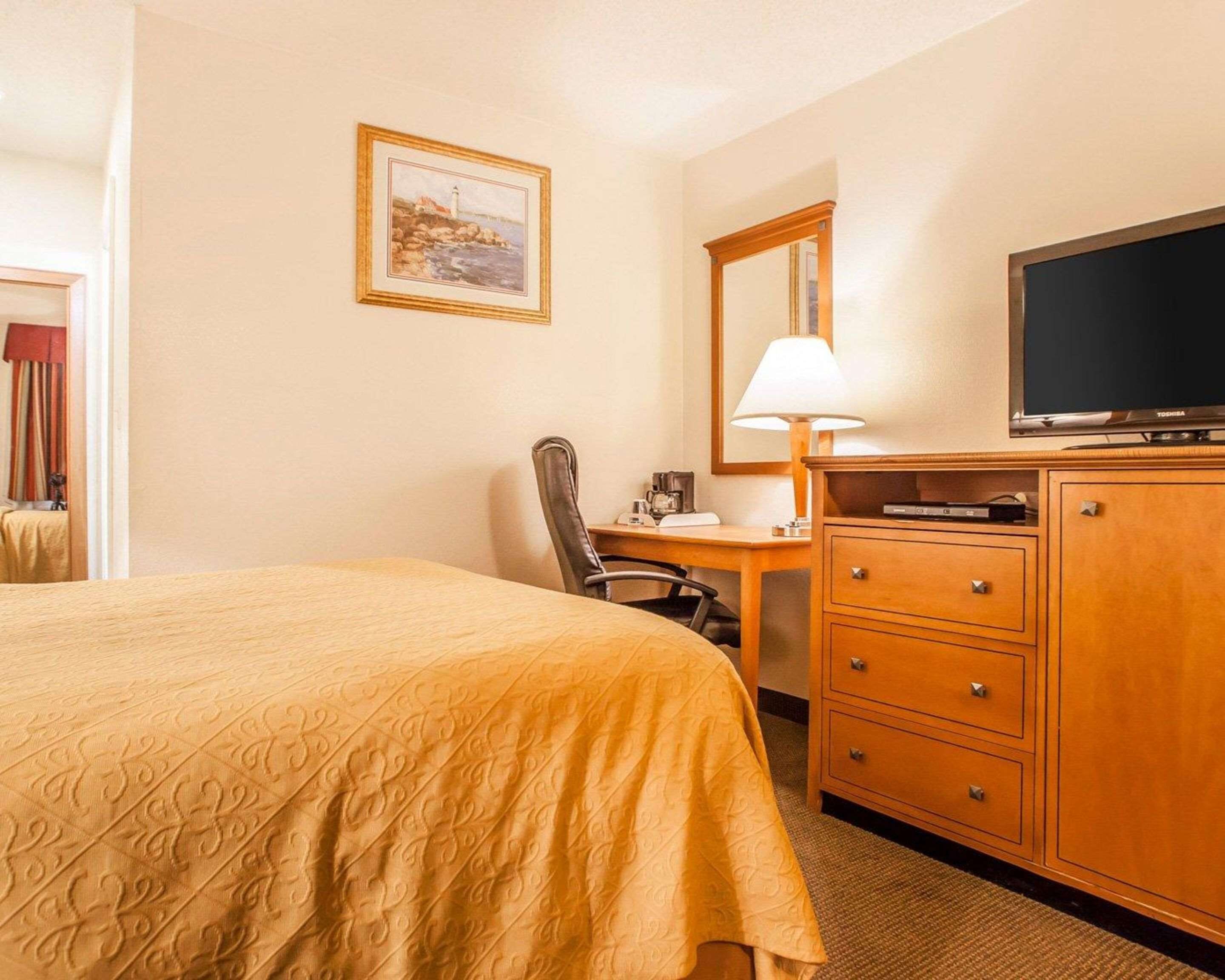 A hotel room with a bed, a desk, a chair, a television, and a cabinet.