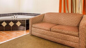 A bathroom with a bathtub, a patterned sofa, and striped curtains. - Rodeway Inn Point Pleasant Beach (Point Pleasant Beach)