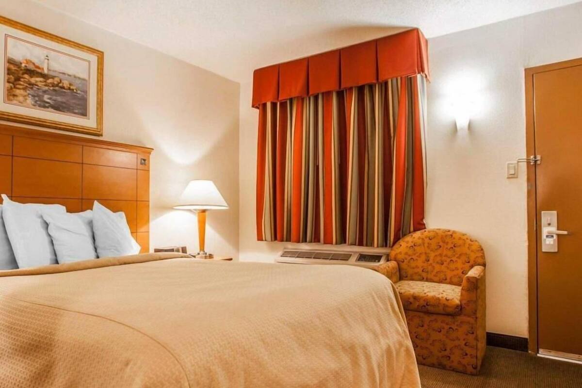 A hotel room with a large bed, a chair, a lamp, a painting on the wall, and a door.