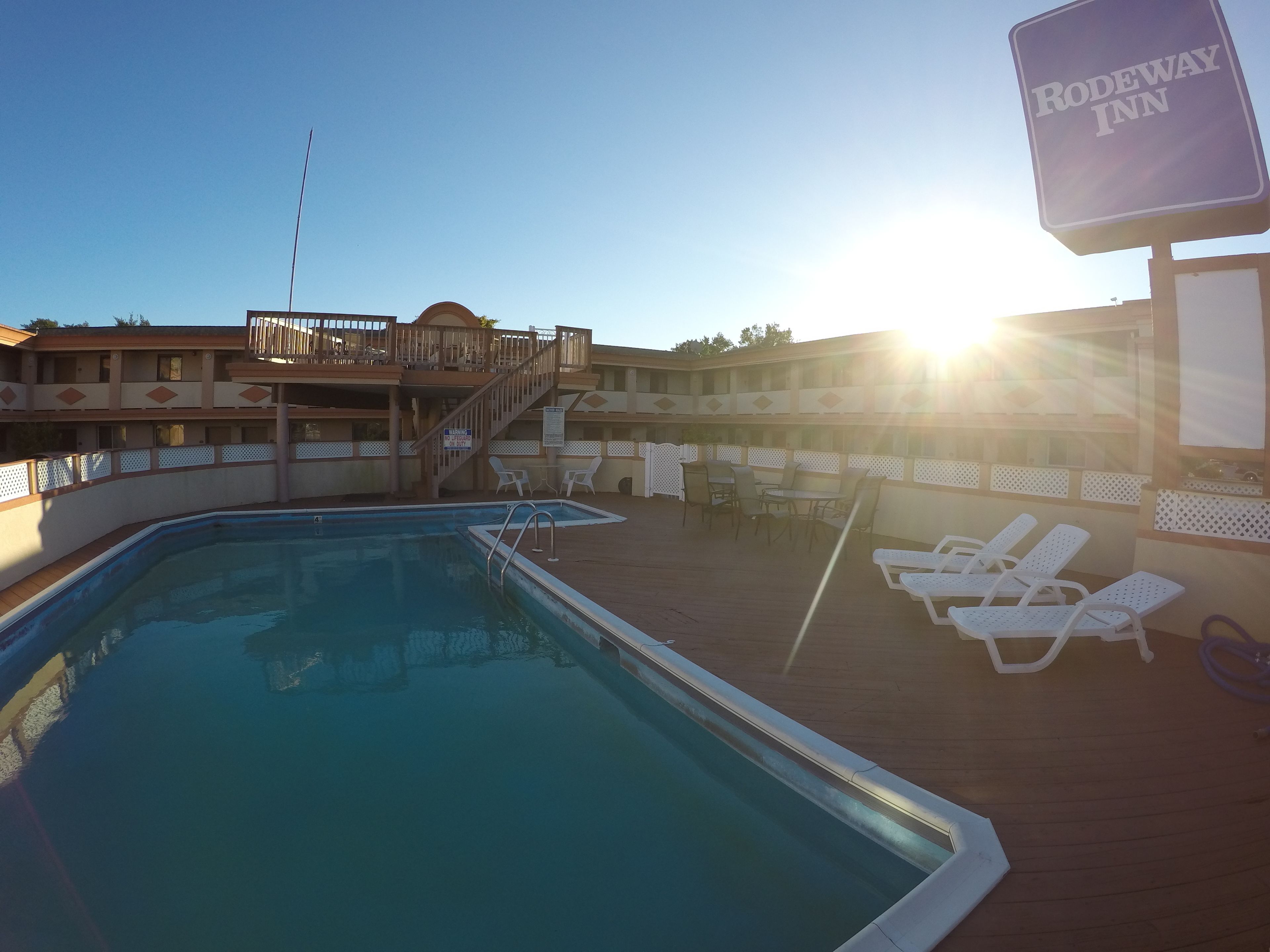 A pool area with lounge chairs and a sign for Rodeway Inn.