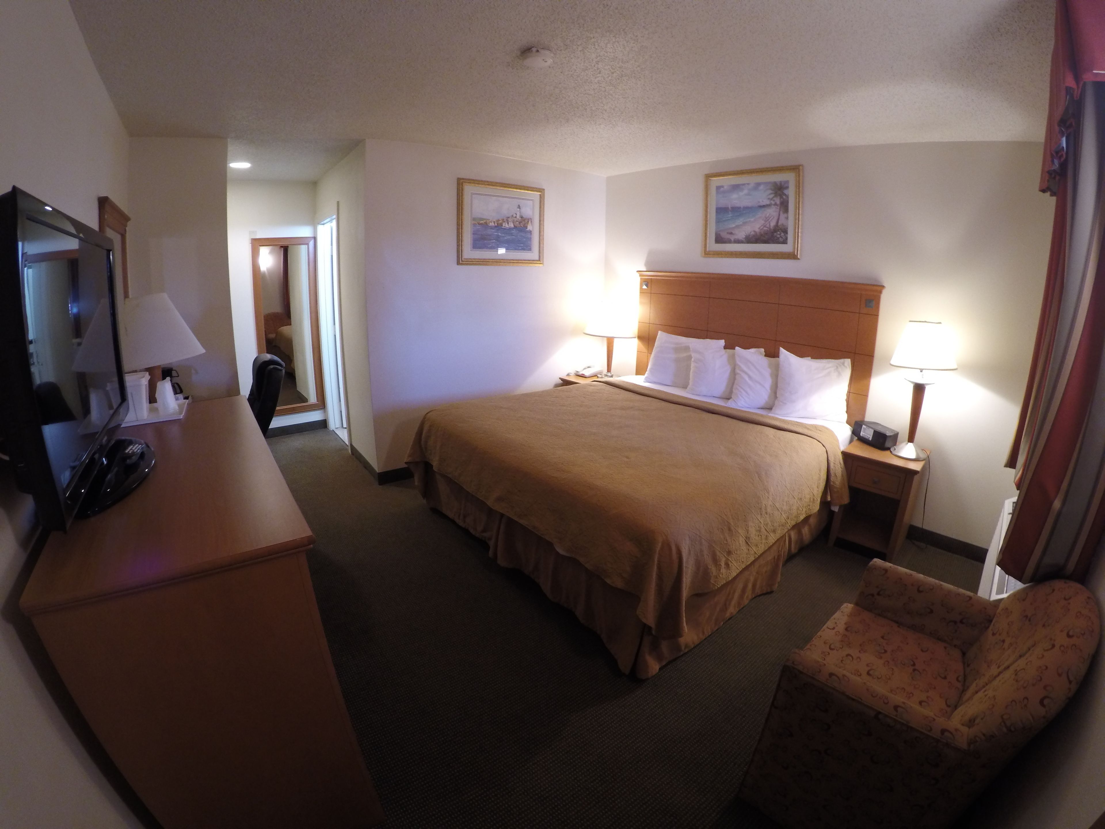 A hotel room with a bed, a desk with a telephone, a chair, and two wall-mounted lamps.