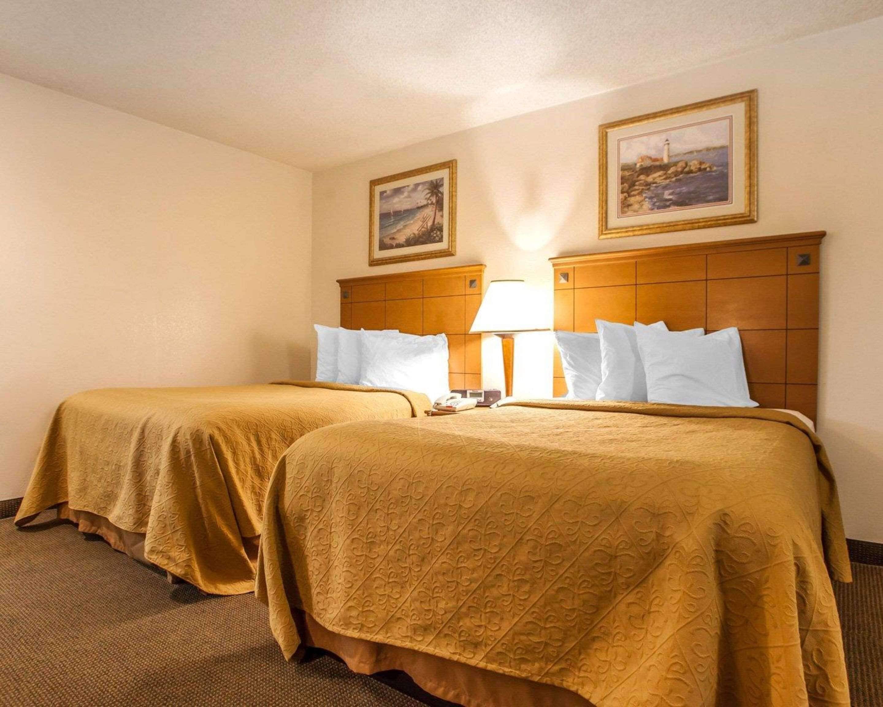 A hotel room with two beds, each with a wooden headboard and a lamp between them.