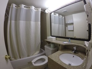 A bathroom with a shower curtain, toilet, sink, and a large mirror.