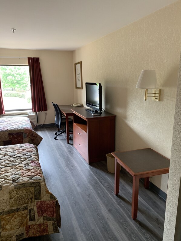 A hotel room with a bed, a desk with a computer, a chair, a TV, and a lamp.