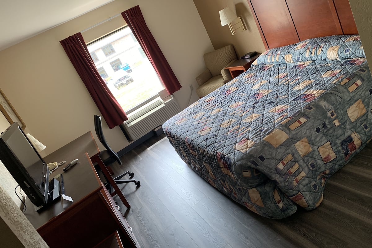 A hotel room with a bed, desk, chair, and a window with curtains.