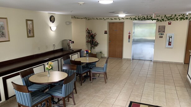 A hotel lobby with a reception desk, seating area with round tables and chairs, a coffee machine, and a fire extinguisher. - Amelia Inn & Suites (Amelia Court House)