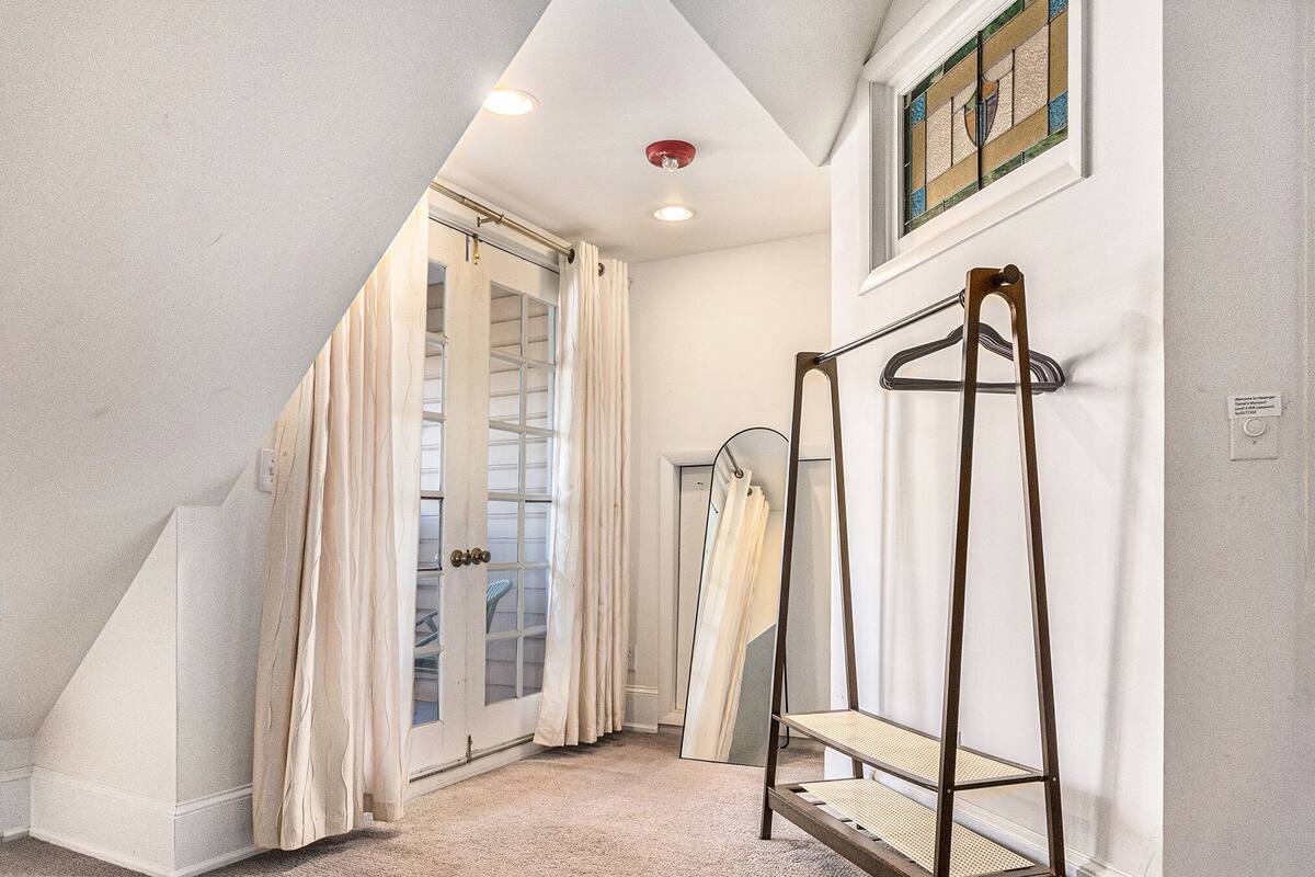 Un couloir étroit avec une porte vitrée donnant sur un balcon, un porte-manteau et un luminaire au plafond.