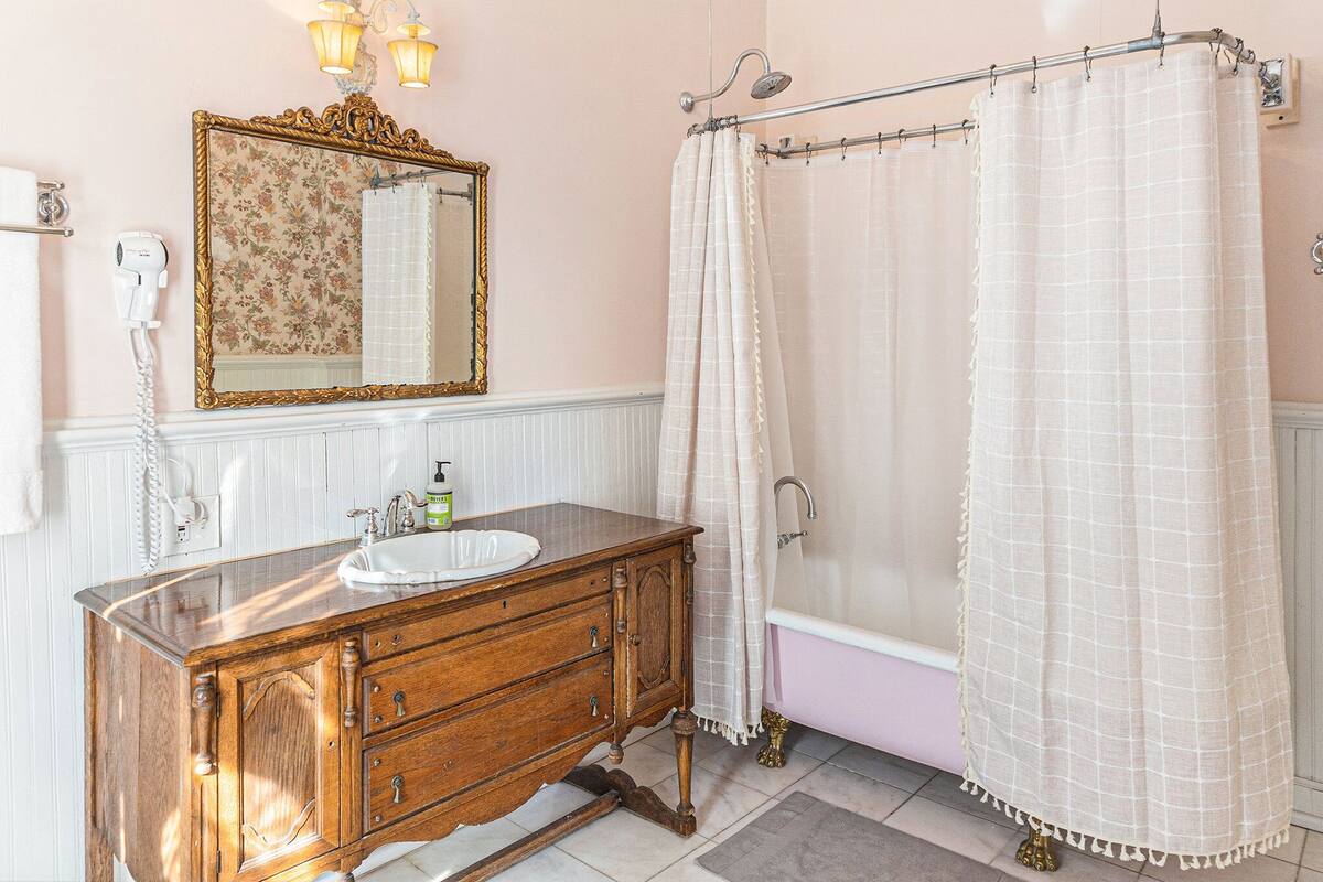 Une salle de bain avec un meuble-lavabo en bois, un lavabo blanc, un miroir avec un cadre floral, un rideau de douche et une baignoire.