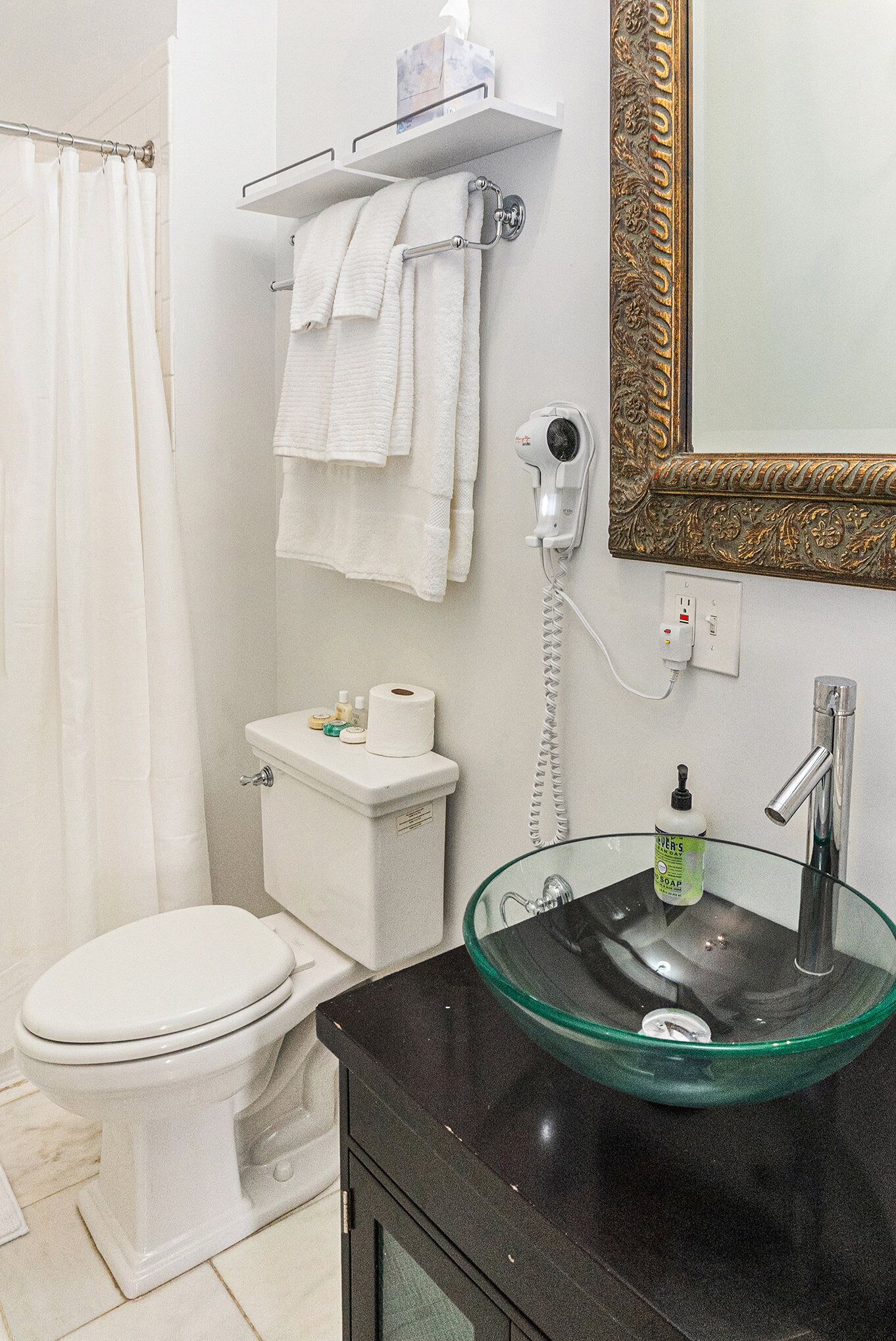 Un baño con lavamanos de vidrio, inodoro blanco y cortina de ducha.