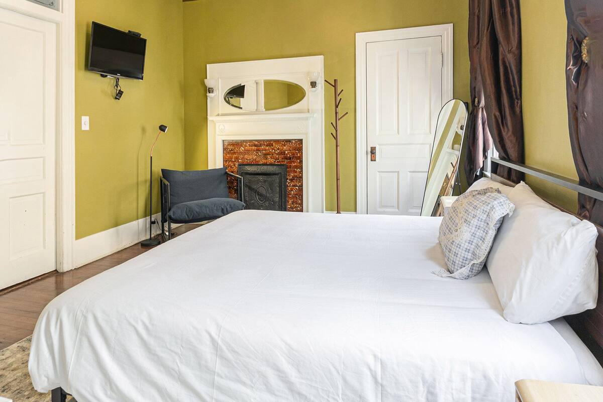 Une chambre à coucher avec un grand lit, une cheminée, un téléviseur fixé au mur et une porte dotée d’un miroir.