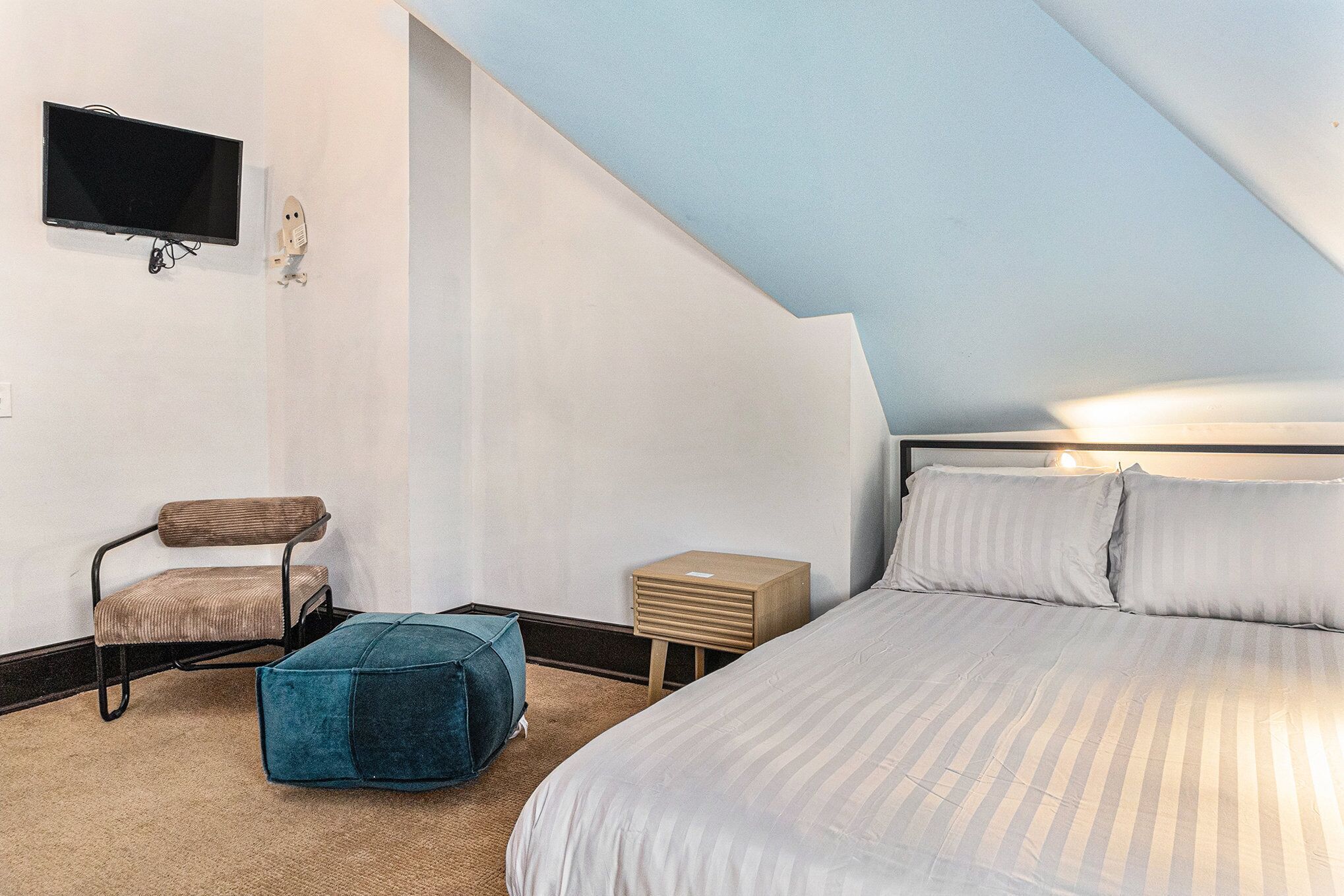 Un dormitorio con una cama, una silla, una mesita y un televisor fijado a la pared.