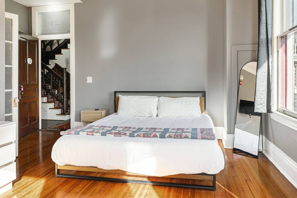 Une chambre à coucher comprenant un lit, une table de chevet, un miroir et un escalier menant à un couloir.