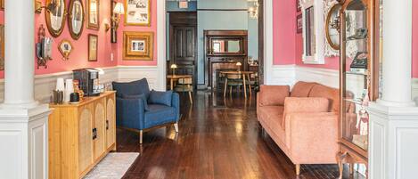 A room with wooden flooring, a blue armchair, a pink sofa, and a wooden cabinet with a mirror.