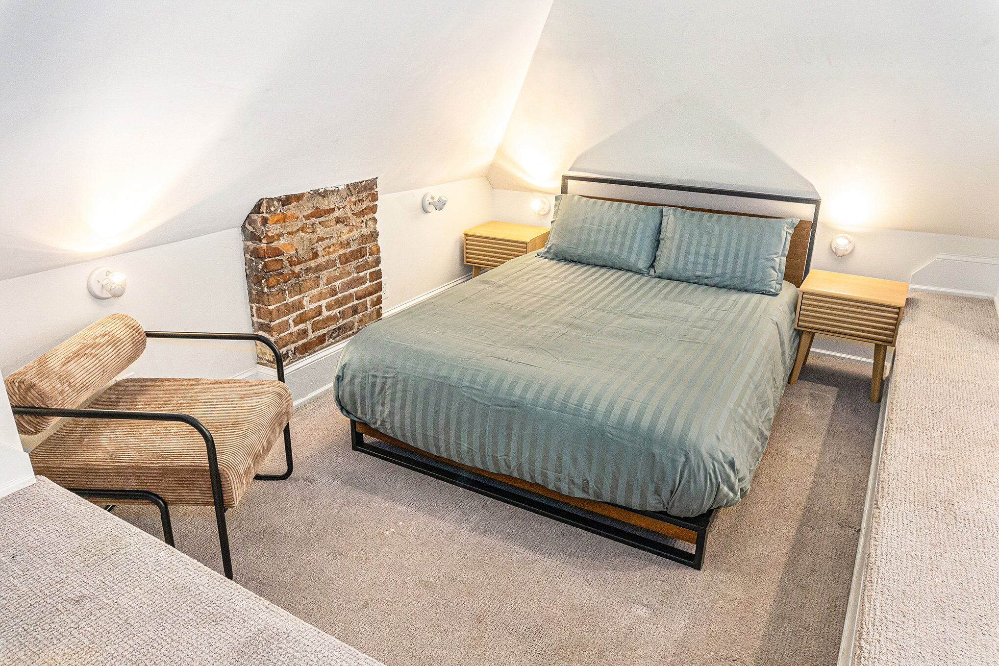 A bedroom with a sloped ceiling, a bed with a wooden frame, a chair, and a small bedside table.