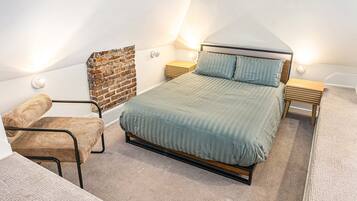 A bedroom with a sloped ceiling, a bed with a wooden frame, a chair, and a small bedside table.