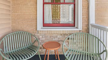 Two green chairs and a small round table outside a building with a brick wall and a window with red trim.