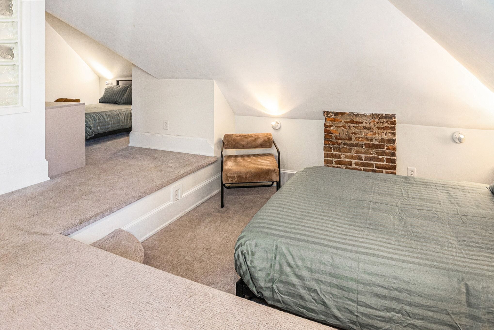 Een slaapkamer met een schuine kap, een bed, een stoel en een klein tafeltje.