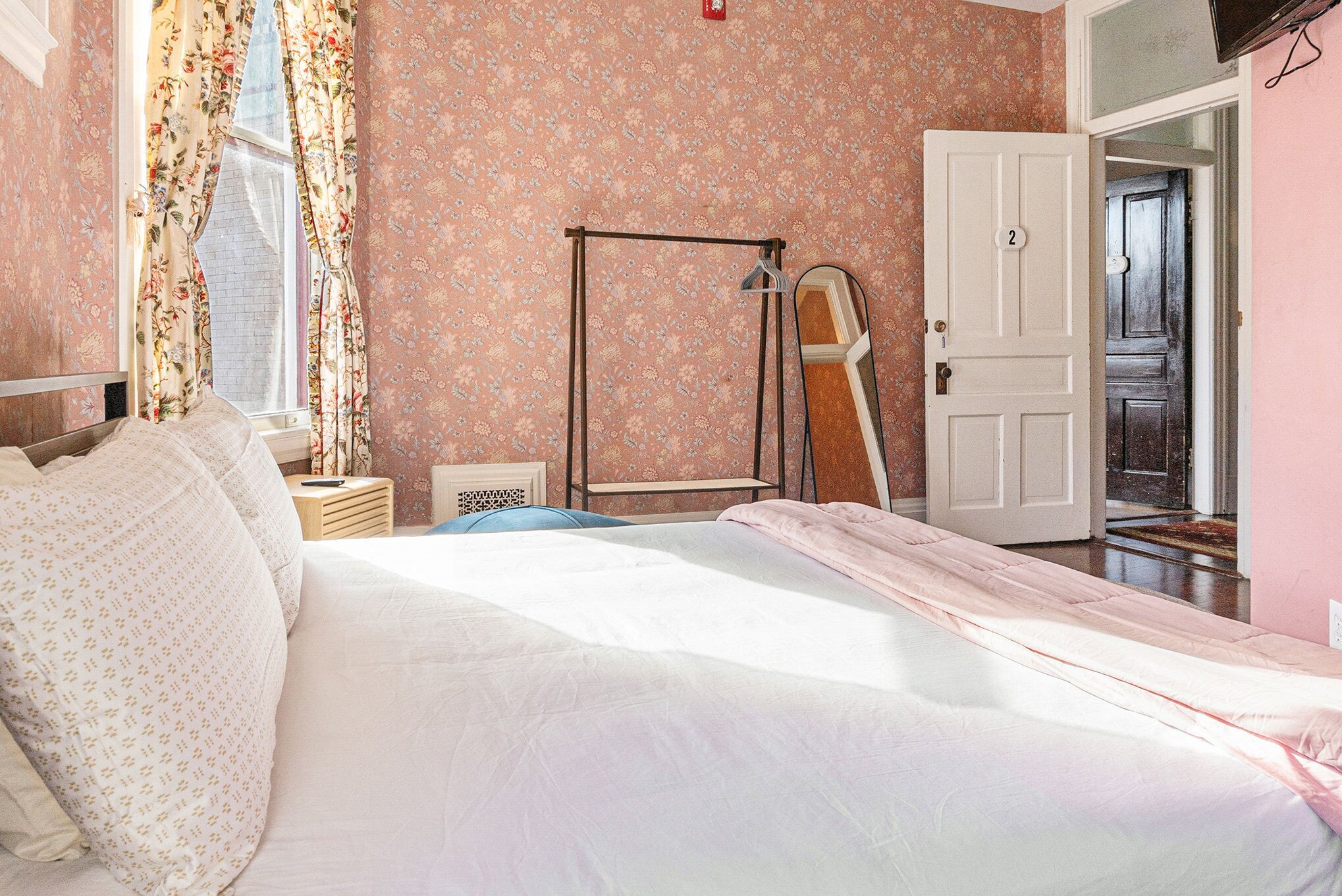 Une chambre à coucher comprenant un lit, une table de chevet, un miroir et une porte donnant sur une autre pièce.