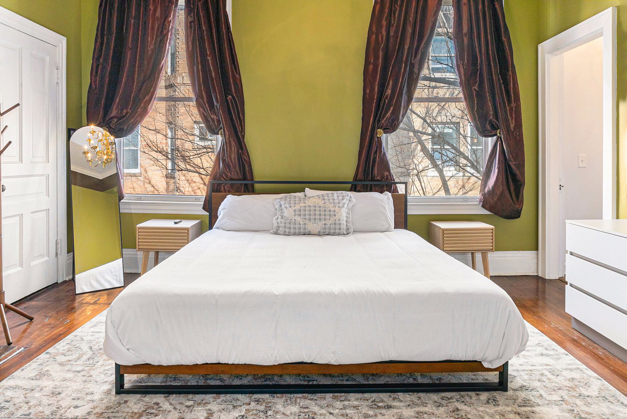 Ein Schlafzimmer mit einem großen Bett, zwei Nachttischen, einem Schminktisch und einem Fenster mit Vorhängen.