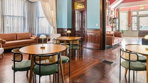 A lobby with a brown leather sofa, round wooden tables, green cushioned chairs, and a wooden floor.
