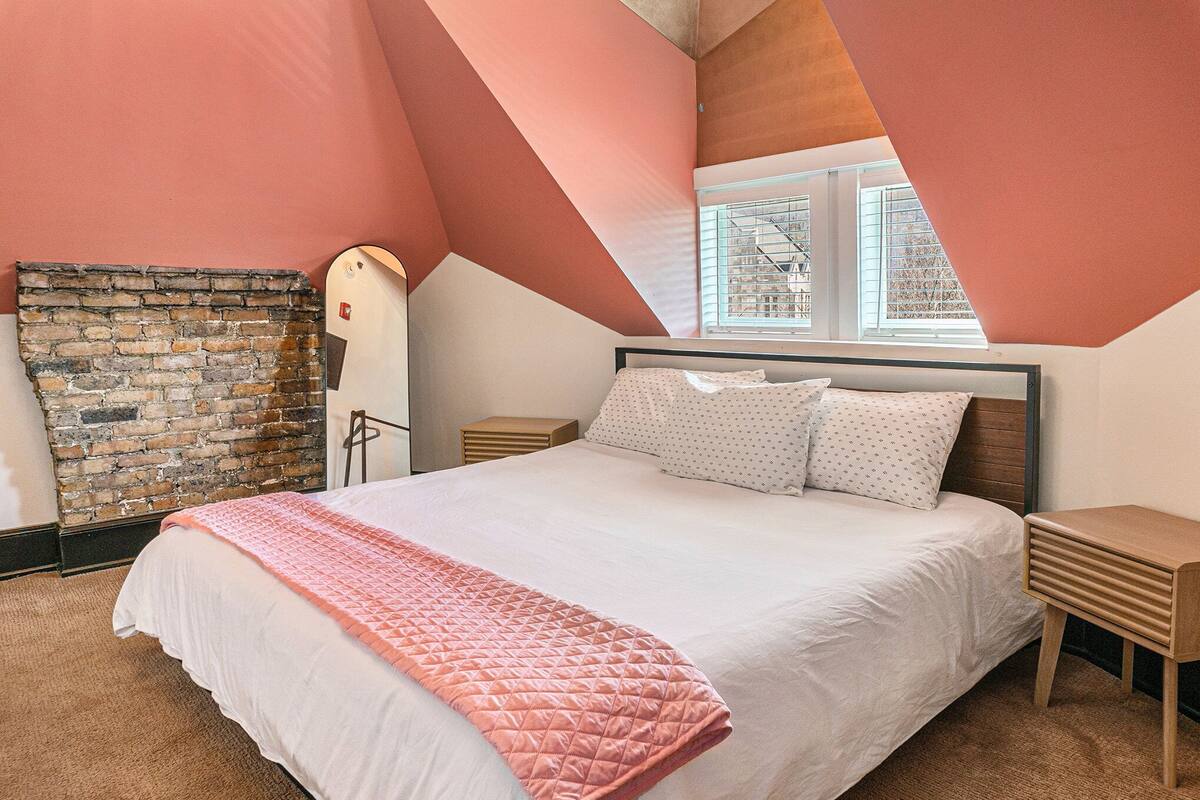 Une chambre avec un grand lit, un mur en briques et une fenêtre donnant sur des immeubles.